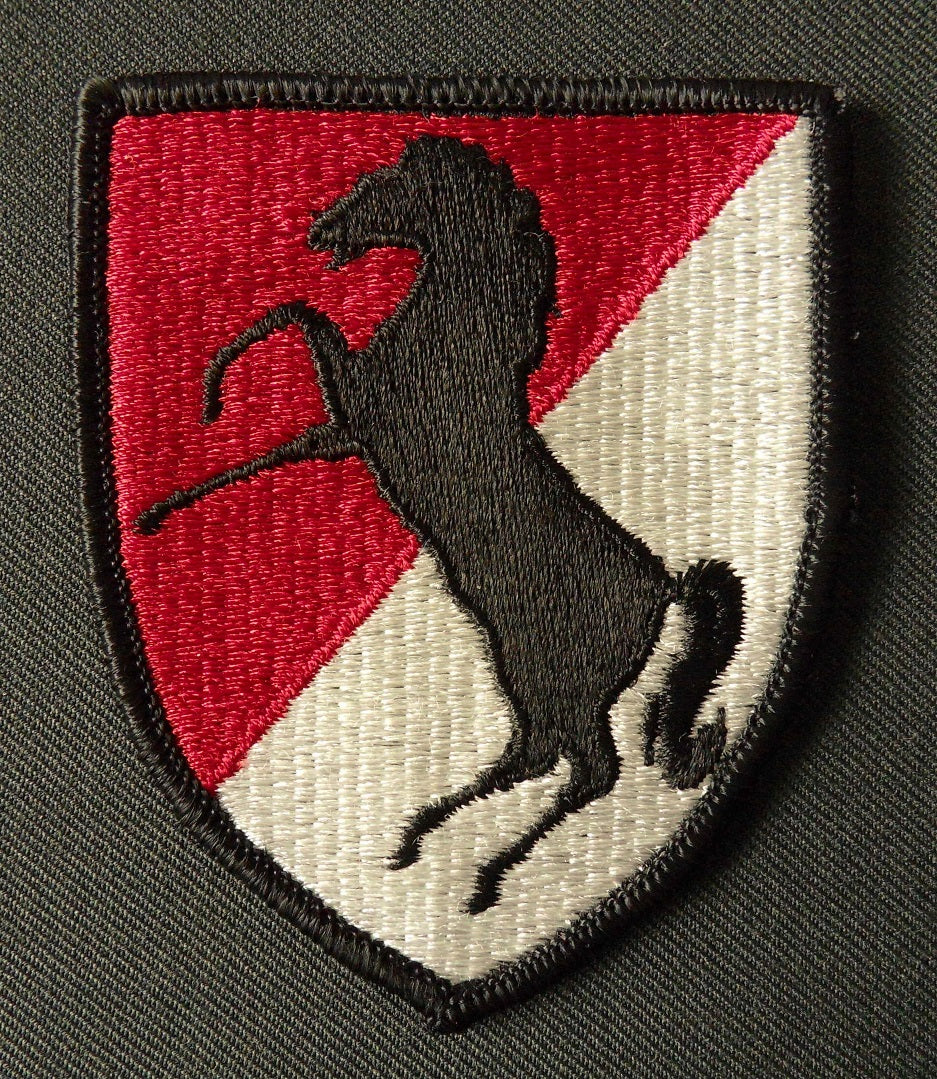 Schildförmiges Patch des 11th Armored Cavalry Regiment der US-Armee in rot und weiß, mit einem springenden schwarzen Pferd in der Mitte