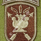 Schildförmiges Patch des JFK Special Warfare Center der US-Armee in Beige und Braun, mit einer antiken Lampe in der Mitte, die von zwei gekreuzten Pfeilen durchzogen wird